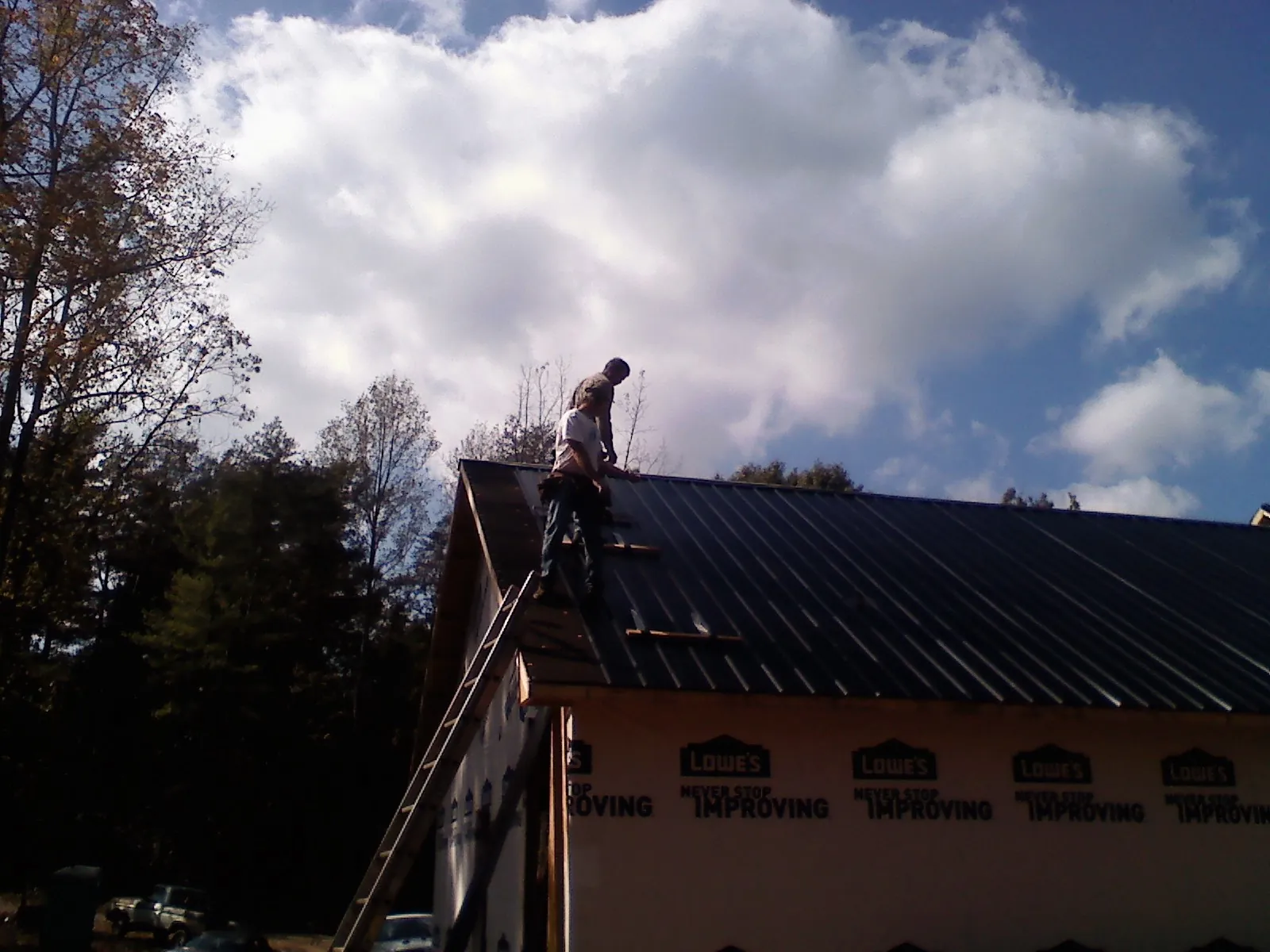 Roofer fastening dark metal panels high against a cloudy sky, from a Roof Inspection job in Rockland